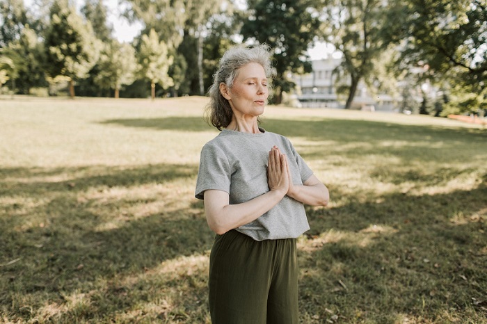 50 year old woman in the park hands in prayer mode, eyes closed, connecting with her spiritual self to find purpose in life after 50