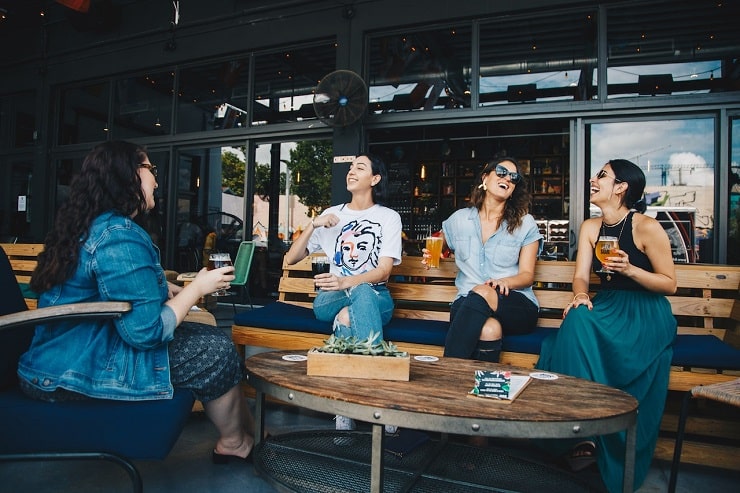 a group of friends sitting down together having lunch on a bench in a restaurant demonstrating social awareness and emotional intelligence by displaying different emotions like smiling, laughing and talking