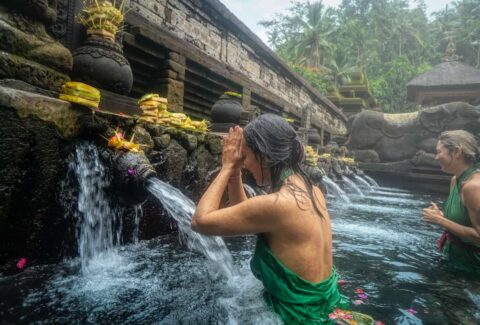 a woman getting purified in Asia in a beautiful spring waterfall for spiritual purification as she navigates through her spiritual awakening stages
