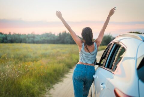 a girl solo traveling in a field with green grass next to her car putting her hands up with the sky with joy, signs you're healing from narcissistic abuse