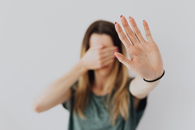 a girl with one hand out saying stop and one hand covering her eyes saying no to set boundaries with a narcissist