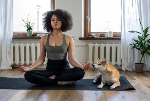 woman on her yoga mat in lotus position with her dog next to her at home doing guided meditation for healing from narcissistic abuse