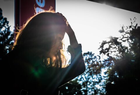 a woman looking down next to a window holding her head in sadness struggling with trauma bond withdrawal symptoms