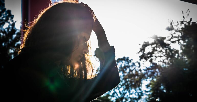 a woman looking down next to a window holding her head in sadness struggling with trauma bond withdrawal symptoms