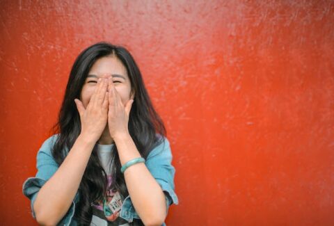 a woman against a red background covering her mouth with her eyes closed laughing at funny things to say to a narcissist