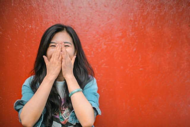 a woman against a red background covering her mouth with her eyes closed laughing at funny things to say to a narcissist