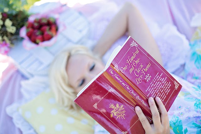 a woman laying in the park on a towel reading a book titled: "one hundred and one love poems"