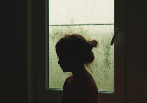 a child sitting in the dark in front of a window