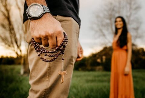 a guy holding christian rosary beads looking at a woman in the park smiling at him