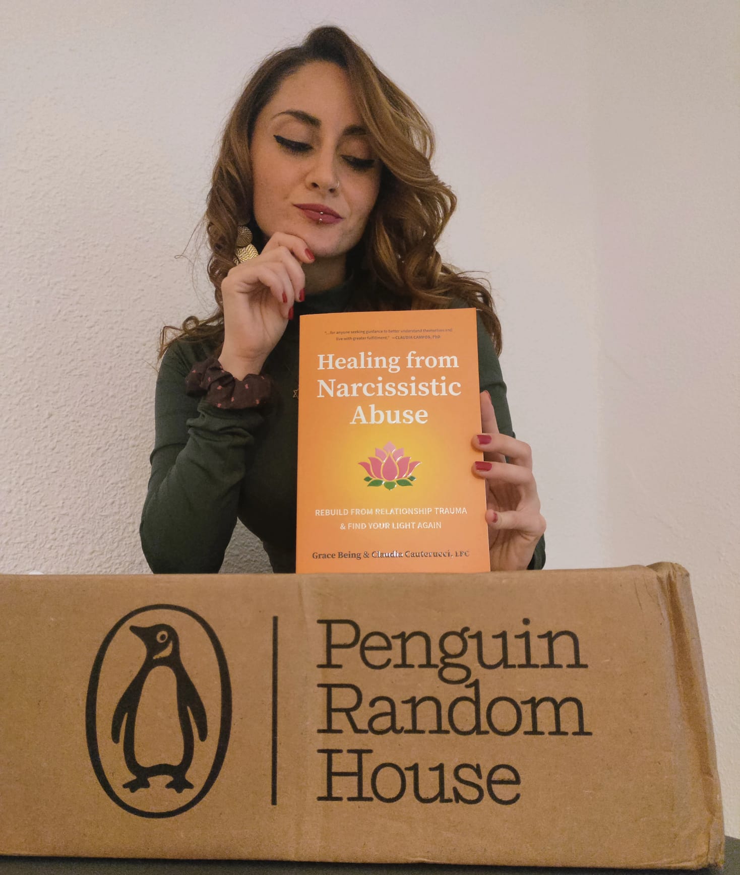 A photo of Grace WILDE Being holding her book in her hands "Healing from Narcissistic Abuse" on a box with the logo of Penguin Random House